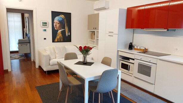 A modern kitchen with white cabinets, a red upper cabinet, and a dining area with a white table and two chairs. - Villa Anna, apartment no. 2 (Venezia)
