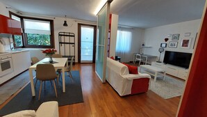 A modern apartment with a kitchen, dining area, and living room. It includes a dining table with chairs, a sofa, a TV, and a sliding glass door leading to a balcony. - Villa Anna, apartment no. 2 (Venezia)