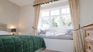 A bedroom with a bed, a window with curtains, a radiator, a bedside lamp, and a dresser. - Holm Oak Lodge (Clacton-on-Sea)