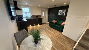 Een moderne keuken met een centraal eiland, een eetgedeelte met een ronde tafel, en een groene bank in een woonkamer.