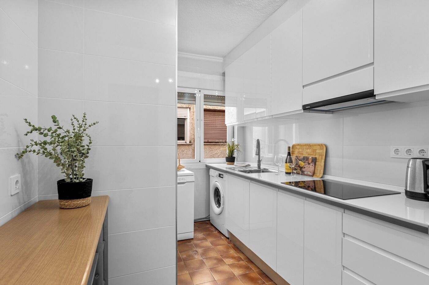 A modern kitchen with white cabinets, a wooden countertop, a washing machine, and a potted plant.