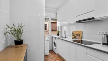 A modern kitchen with white cabinets, a wooden countertop, a washing machine, and a potted plant.