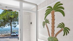 A room with a tiled floor, a large window with a view of a tree and a car outside, and a wall with a palm tree mural.