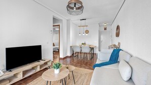 A modern living room with a flat-screen TV, a sofa, a coffee table, and a dining area with a table and chairs.