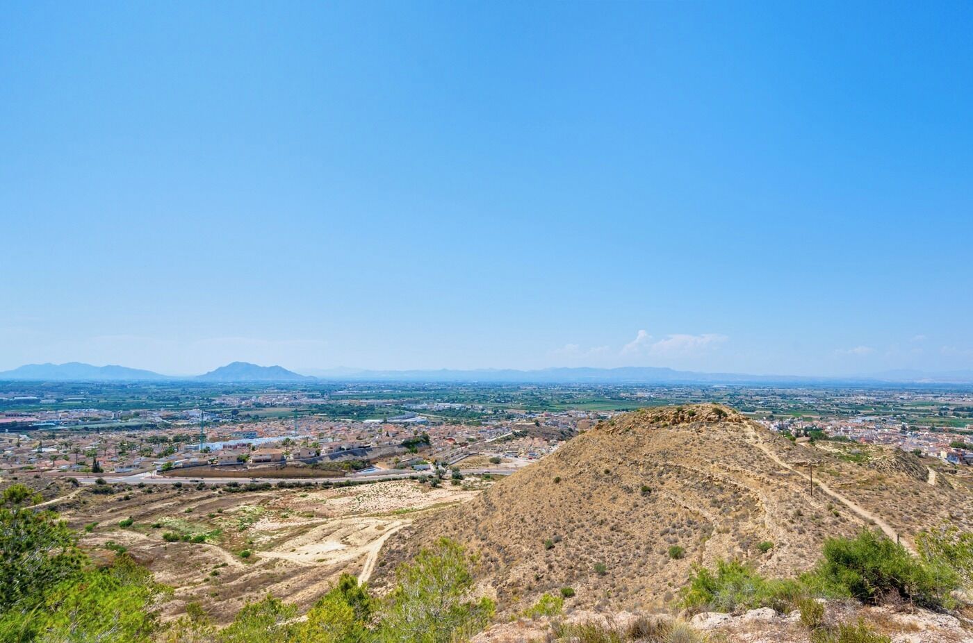 A panoramic view of a city with a prominent hill in the foreground and distant mountains.