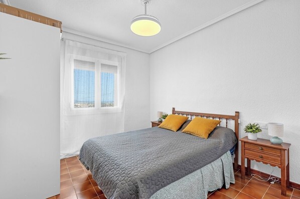 Un dormitorio con una cama, una mesita de noche, una lámpara y una ventana.