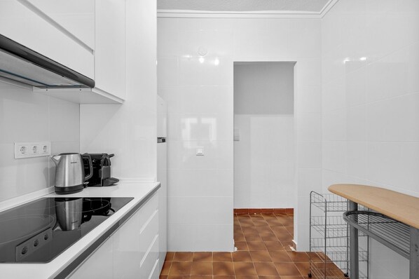 A modern kitchen with white cabinets, a black countertop, a kettle, a coffee maker, and a wooden bench.