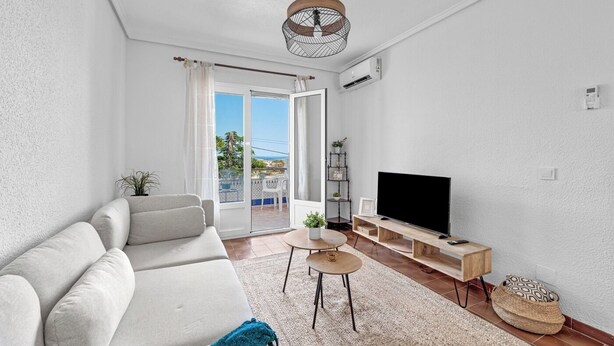 A modern living room with a sofa, a TV on a wooden stand, a small table, and a balcony with a view.