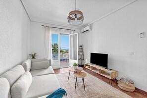 Una sala de estar moderna con un sofá, un televisor sobre un mueble de madera, una mesita y un balcón con vistas.