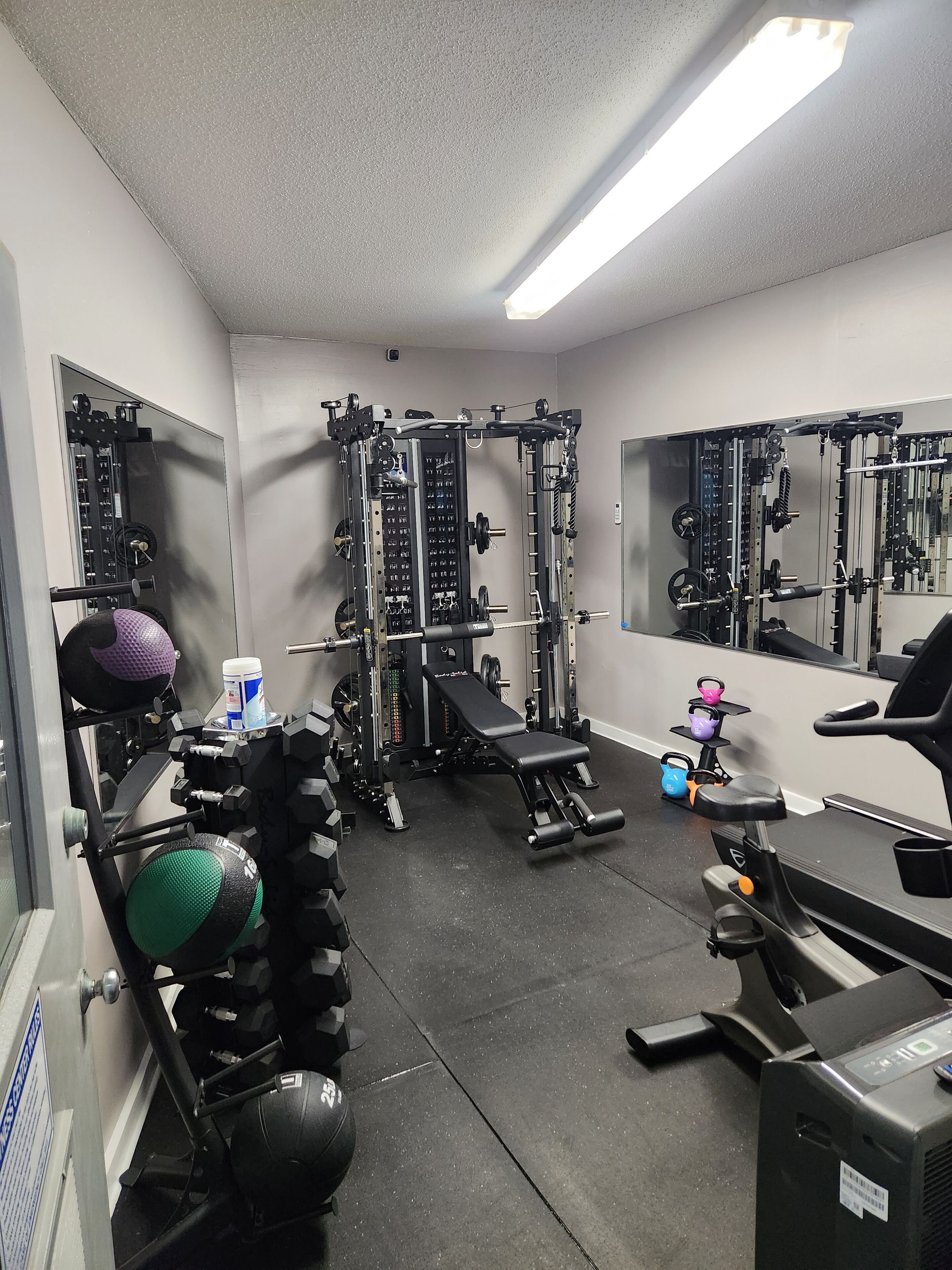 A gym with various exercise equipment, including a squat rack, bench press, and kettlebells.