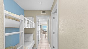 Un pasillo estrecho con literas a un lado y una puerta que da a otra habitación al otro.