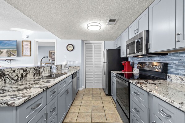 A modern kitchen with grey cabinets, a granite countertop, a stainless steel refrigerator, and a microwave.