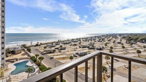 A view of a parking lot with RVs and a swimming pool, overlooking a beach and ocean.