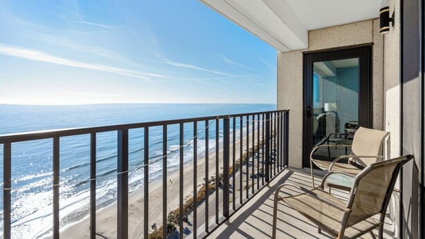 A balcony with a view of the ocean, a chair, and a door leading to a room.