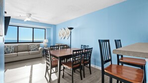 A room with a dining table, chairs, a sofa, and a view of the ocean.