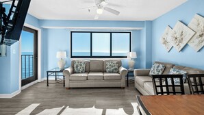 A living room with a sofa, two side tables, a ceiling fan, and a view through a large window.
