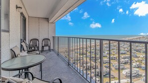 Un balcón con mesa y sillas, con vista a la playa y un estacionamiento.