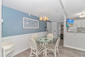 A dining area with a glass-top table surrounded by wicker chairs, a decorative wall piece, and a ceiling light fixture.
