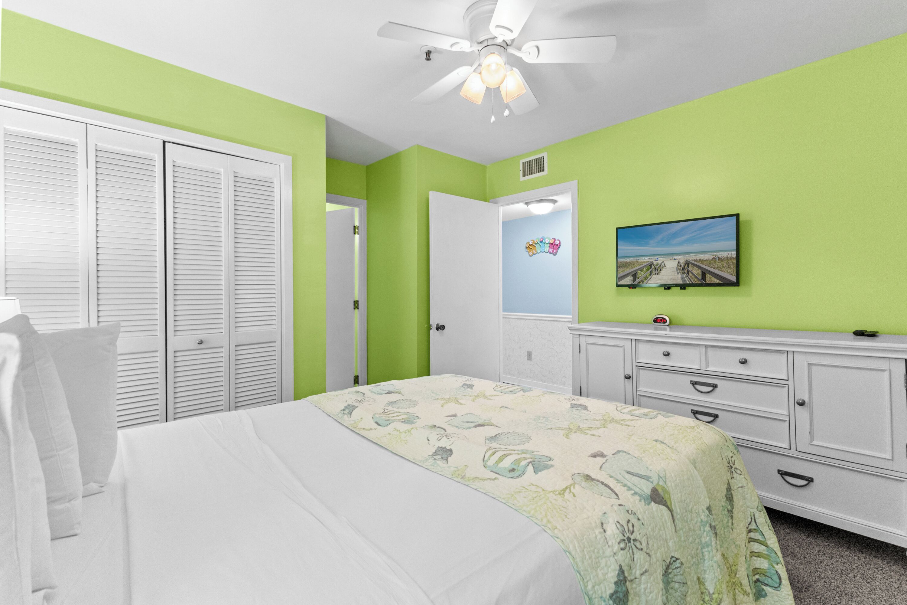 Une chambre à coucher comprenant un lit, un ventilateur de plafond, une commode, un téléviseur et un placard.