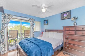 Une chambre à coucher avec un lit, une commode, un ventilateur de plafond et une fenêtre avec des rideaux.