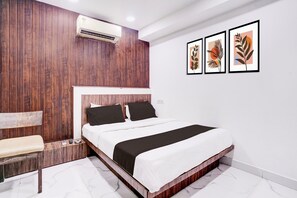 Een slaapkamer met een houten hoofdbord, een bed met wit en zwart beddengoed, een bankje en drie ingelijste kunstwerken aan de muur.