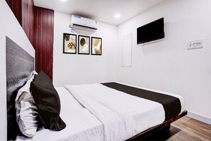 Een slaapkamer met een bed, een wandtelevisie, een airconditioner en drie ingelijste kunstwerken aan de muur.