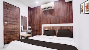 A modern hotel room with a wooden panel wall, a large bed with white and black bedding, a chair, and a desk with a lamp. - Comfy Stays at Lokhandwala Andheri West (Mumbai)