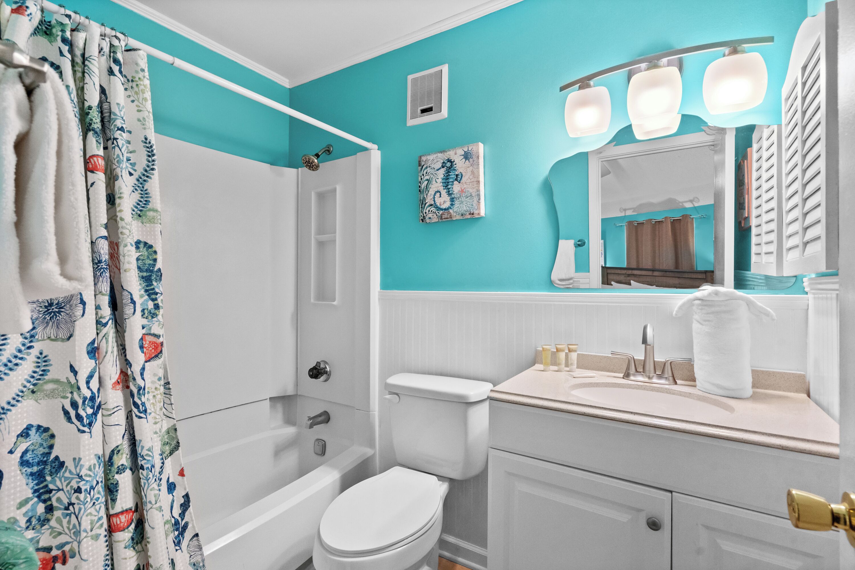A bathroom with a white toilet, a bathtub, a sink with a mirror, and a shower curtain with a floral pattern.