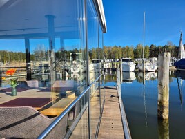 Un puerto deportivo con barcos amarrados, una terraza de madera y una barandilla de cristal con vistas al agua.