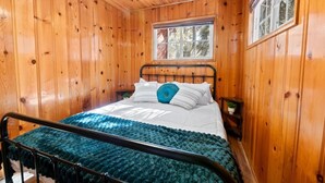 A wooden-paneled bedroom with a bed, a window, and a nightstand.