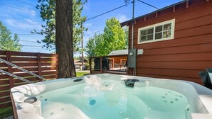 A hot tub in a backyard with a wooden fence, a tree, and a house in the background.