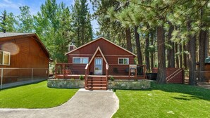 A rustic cabin with a stone foundation, a wooden deck, and a concrete pathway leading to the entrance.