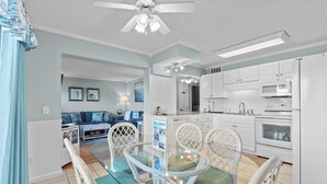 A modern kitchen with white cabinets, a microwave, and a refrigerator. There is a dining area with a glass table and white chairs. - Myrtle Beach Resort A0327 (Myrtle Beach)