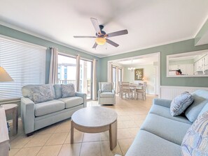 A living room with a sofa, a coffee table, a ceiling fan, and a view to the outside.