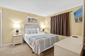 Une chambre d’hôtel avec un lit, deux lampes de chevet, une table de chevet, un bureau, un rideau marron et un tableau encadré au mur.