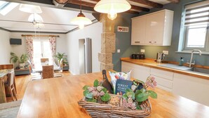 A dining area with a wooden table, wicker basket with snacks, and a kitchen in the background. - New Elms Farmhouse (Derby)