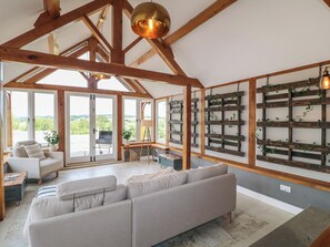 Un vaste espace de vie doté d’un plafond haut et de poutres en bois, d’un grand canapé et d’une vue imprenable sur l’extérieur grâce à de grandes fenêtres.