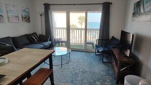 A living room with a sofa, a coffee table, a TV, and a balcony with a view of the sea. - Private Bayview Condo (Corpus Christi)