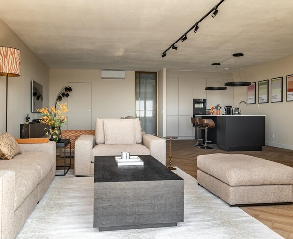 A modern living room with a sofa, a coffee table, and a kitchen area in the background.