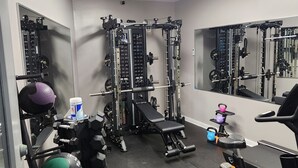 Ett gym med olika typer av träningsutrustning, inklusive en knäböjsställning, en bänkpress och kettlebells.