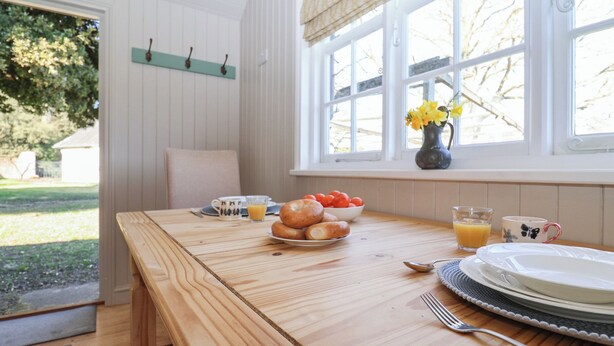 Un tavolo da pranzo in legno con articoli per la colazione, una finestra con vista sugli alberi e una porta che dà sull'esterno.