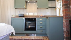 Una cucina compatta con mobili color petrolio, forno a incasso e lavello con rubinetteria dorata.