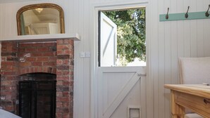 Una stanza con un camino in mattoni, una porta bianca con finestra, un tavolo di legno e un tappeto decorato.