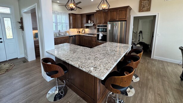 Una cocina amplia con una isla grande, armarios de madera oscura, electrodomésticos de acero inoxidable y una encimera de granito.