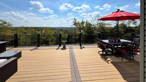 Una terraza de madera con una mesa, sillas y un paraguas rojo, y vistas a un área boscosa.