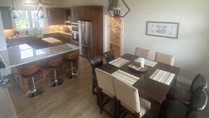 Una cocina moderna con electrodomésticos de acero inoxidable, un comedor con mesa y sillas de madera, y un letrero que dice "WELCOME TO OUR NEST".