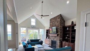 Un salón espacioso con techo alto, chimenea de piedra y un televisor grande.