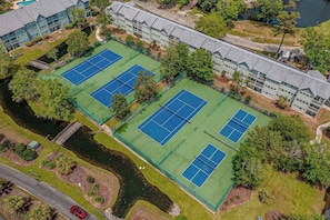 Ett flygbildsfoto av ett hotell med flera tennisbanor, en flod och en parkeringsplats.