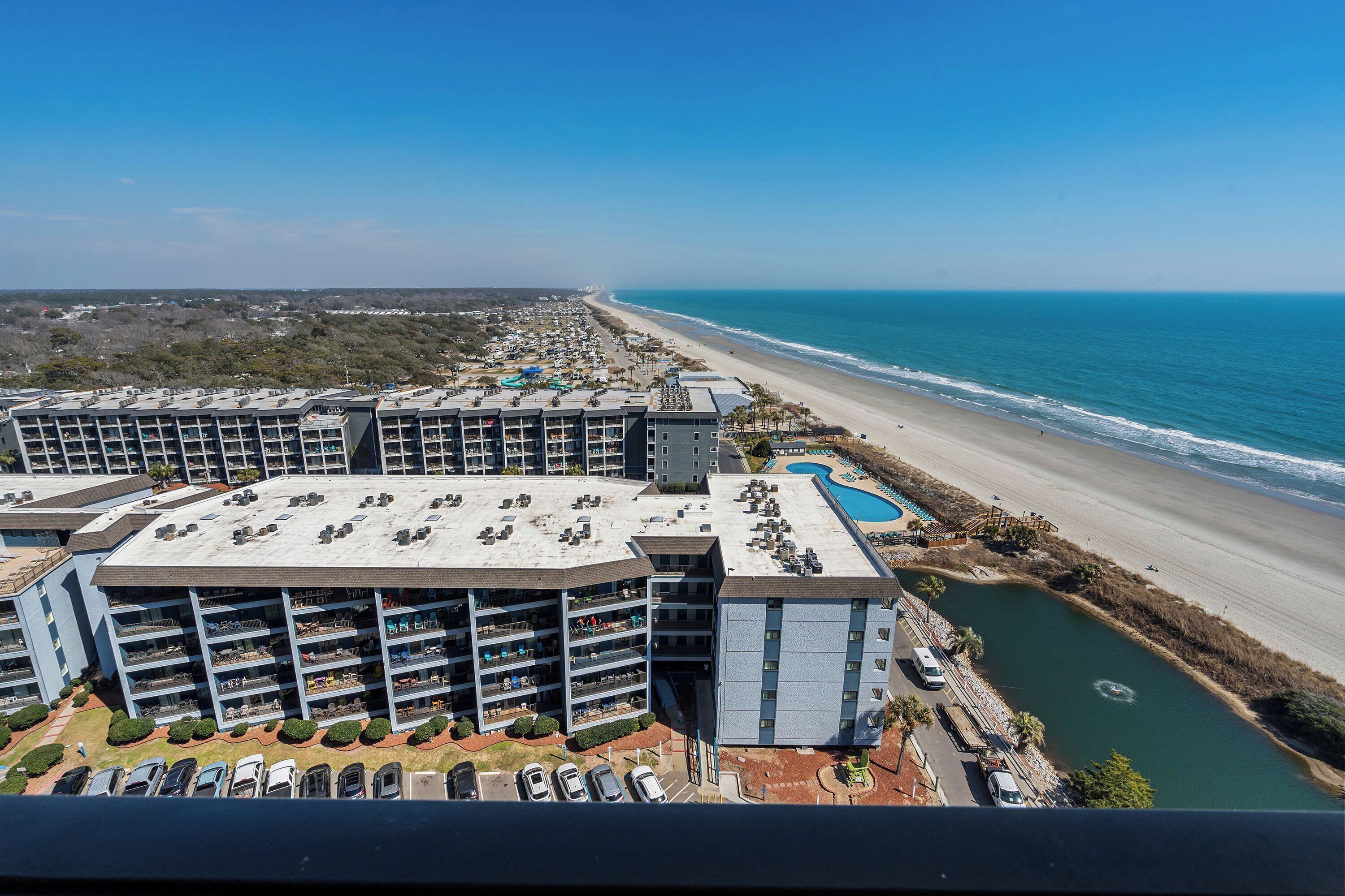 A high-rise hotel with multiple balconies, a swimming pool, and a beach view.