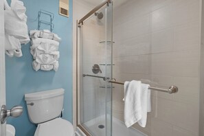 A bathroom with a toilet, a glass shower enclosure, and a towel rack with folded towels. - Myrtle Beach Resort RT1104 (Myrtle Beach)
